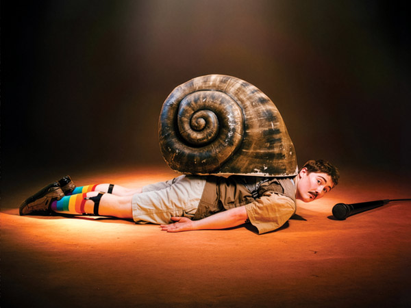 Publicity image of Bi Curious George lying on the floor underneath a snail shell