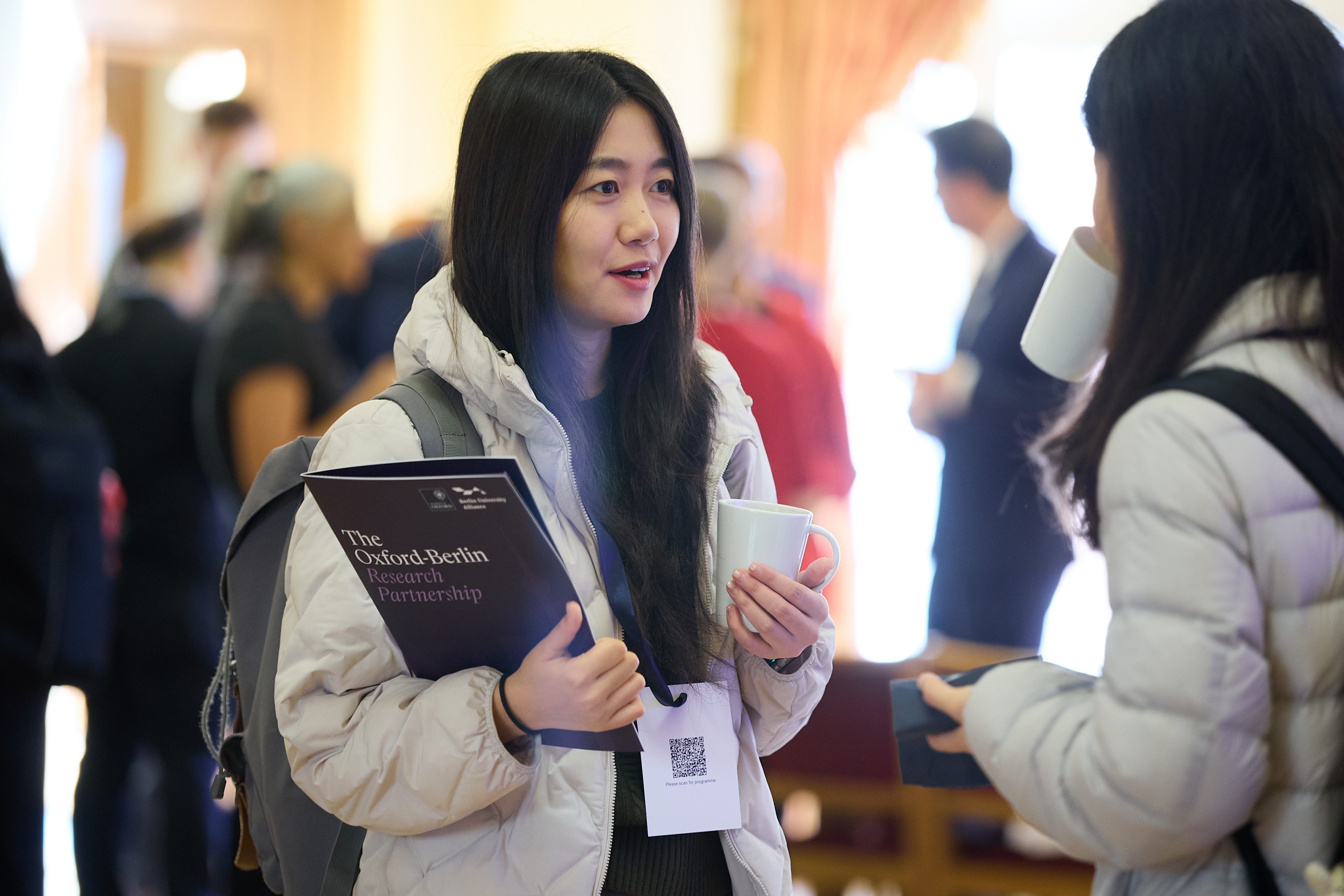 Two female researchers in conversation, one holding an Oxford Berlin Research Partnership brochure
